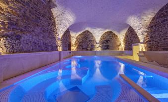 a large indoor swimming pool surrounded by stone walls , with a blue light illuminating the water at Monastero di Cortona Hotel & Spa