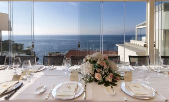 a table set for a formal dinner , with white tablecloth and flowers , overlooking the ocean at Hotel Continental