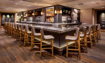 a modern bar with a marble counter and wooden chairs , surrounded by a variety of liquor bottles at Marriott Boston Quincy