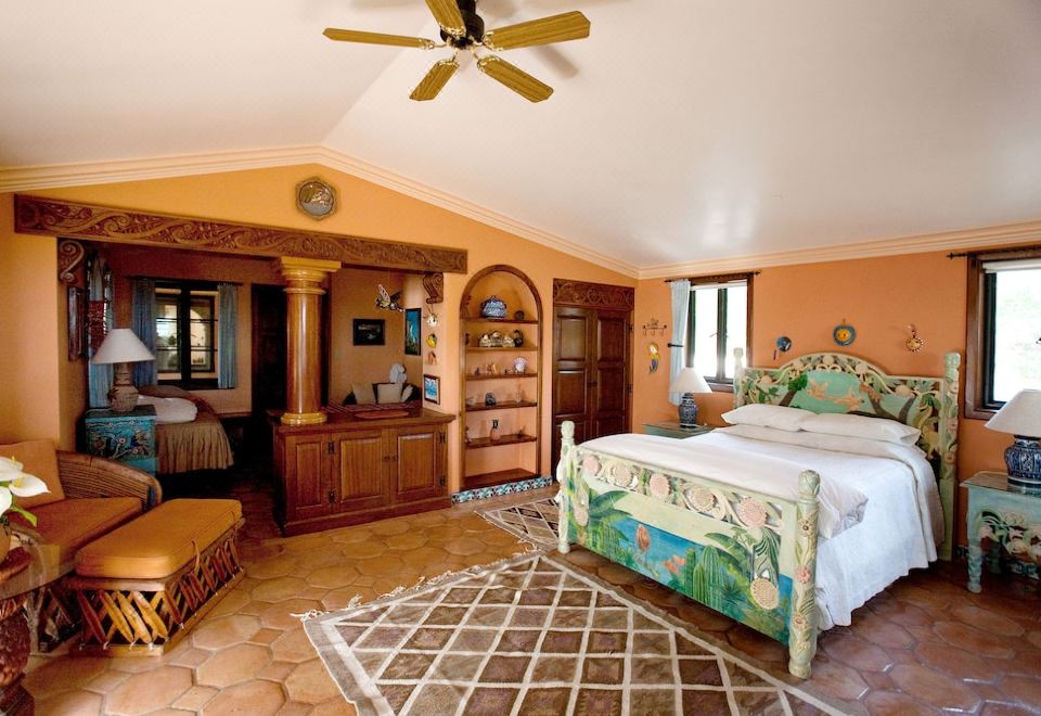 a spacious bedroom with an ornate bed , hardwood floors , and an orange accent wall , along with a fan and bookshelf at Villa del Faro