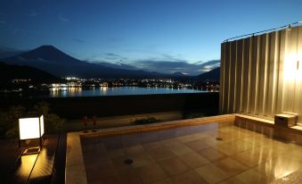 a rooftop terrace with a hot tub , overlooking a lake and mountains at night , under the glow of lights at Mizno Hotel