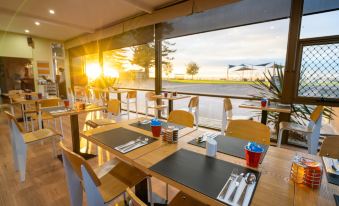 a restaurant with wooden tables and chairs , along with a view of the ocean through large windows at Hospitality Esperance, SureStay Collection by Best Western