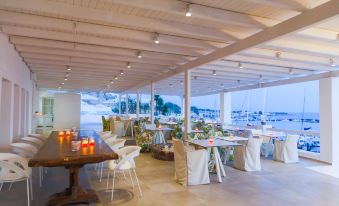 a restaurant with white tables and chairs , set for a gathering , is situated under a covered area at Notos Therme and Spa