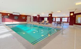 an indoor swimming pool with a diving board , surrounded by chairs and tables , in a spacious room with red walls at Homewood Suites by Hilton Bloomington