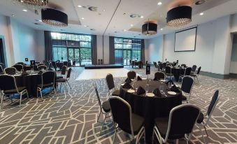 a large , well - lit conference room with multiple tables and chairs arranged for a meeting or event at Village Hotel Farnborough
