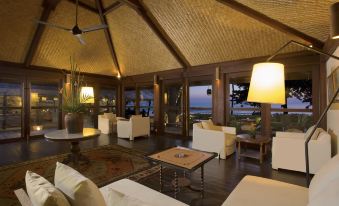 a spacious living room with a thatched roof , white furniture , and a view of the ocean at Jeeva Klui Resort