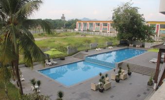 a large outdoor swimming pool surrounded by a grassy field , with several lounge chairs and umbrellas placed around the pool area at Impiana Hotel Ipoh