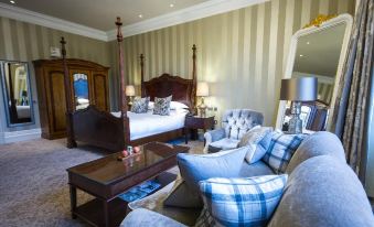 a spacious bedroom with a large four - poster bed , blue and white checkered couch , and striped walls at Bovey Castle