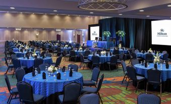 a large banquet hall with blue tables and chairs , a stage at the front , and a stage in the background at Hilton Lexington/Downtown