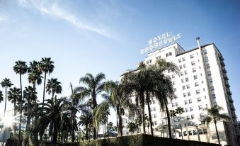 a tall building with a sign on top , surrounded by palm trees and other vegetation at The Hollywood Roosevelt