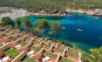 a beautiful coastal area with clear blue water , green trees , and white umbrellas on a terrace at Ole Galeon Ibiza