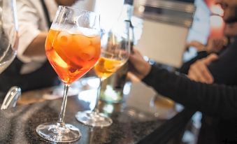 a man is standing behind a bar counter , holding a wine glass filled with orange - colored liquid at Hotel Plaza