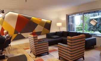 a modern living room with colorful furniture , including a couch and chairs , surrounded by windows at Mercure Castres l'Occitan