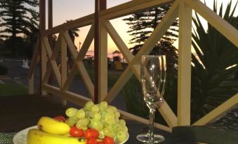 a dining table with a plate of fruit , a glass of wine , and a cup on it at Brighton Beachfront Holiday Park Adelaide