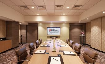 a conference room with a large table , chairs , and a screen displaying the hilton garden inn logo at Hilton Garden Inn Puchong