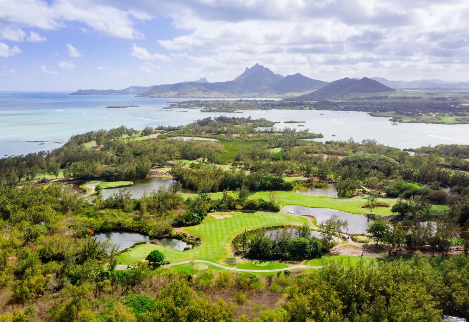 aerial view of a golf course with lush green grass , trees , and water bodies in the background at Four Seasons Resort Mauritius at Anahita