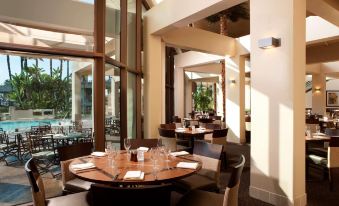 a restaurant with several tables and chairs , each table having white plates and wine glasses , is set up near large windows at Hyatt Regency Long Beach