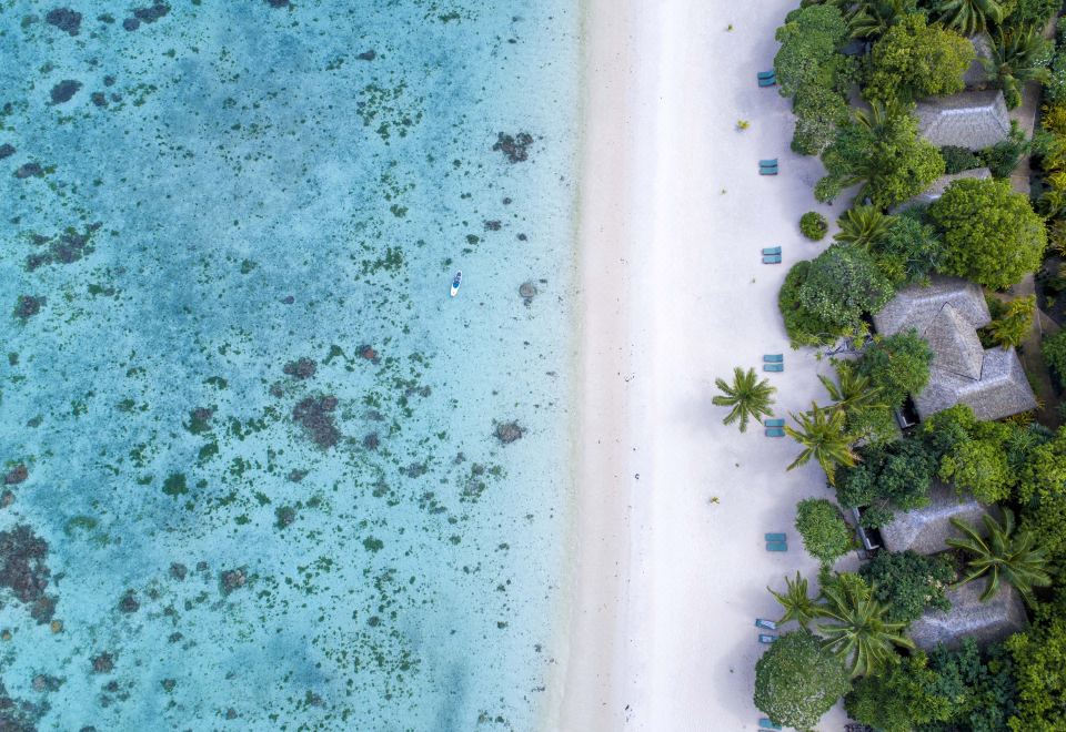 aerial view of a tropical island beach with white sand , clear blue water , and palm trees at Small Luxury Hotels of the World - Pacific Resort Aitutaki