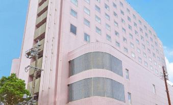 a large pink building with a triangular window design is surrounded by trees and has a clear blue sky in the background at Hotel Resol Gifu