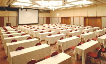 a large conference room with multiple rows of tables and chairs , a projector screen , and chandeliers hanging from the ceiling at Hotel Nikko Kansai Airport