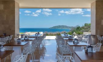 an outdoor dining area with white chairs and tables , overlooking a body of water and mountains at Wyndham Tamarindo