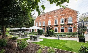 a brick building surrounded by a lush green garden , with tables and chairs set up for outdoor dining at The Knaresborough Inn - the Inn Collection Group
