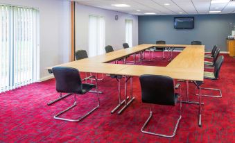 a large conference room with a wooden table , black chairs , and a red carpet , surrounded by white walls and windows at Ibis Styles Barnsley