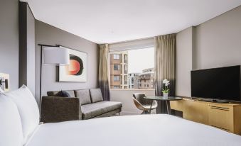 a hotel room with a large window , white bed , and a couch , along with a tv and other amenities at Novotel Sydney Darling Harbour