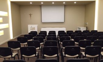 a conference room with rows of black and white chairs , a projector screen , and a podium at Hotel Leone
