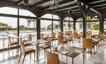 a modern restaurant with wooden tables and chairs , large windows , and a view of the pool at Ilunion Hacienda de Mijas