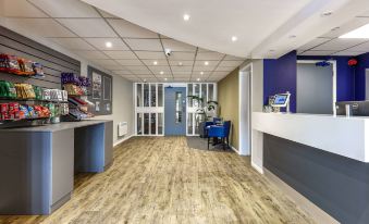 a modern office space with a reception area , wooden flooring , and blue walls , featuring a blue door , white walls , and a wooden desk at Days Inn by Wyndham London Stansted Airport