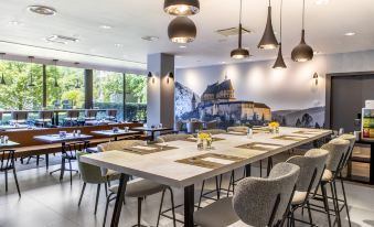 a modern restaurant with a long dining table and chairs , surrounded by windows and a mural on the wall at NH Luxembourg