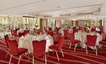 a large , empty banquet hall with red chairs and white tablecloths , set for a formal event at Park Plaza Leeds