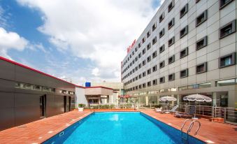 a large swimming pool is surrounded by lounge chairs and umbrellas , with a tall hotel building in the background at Ibis Lagos Ikeja
