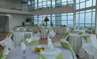 a large , empty banquet hall with white tablecloths and chairs , decorated with green napkins and flowers , set against a backdrop of at Cikidang Plantation Resort