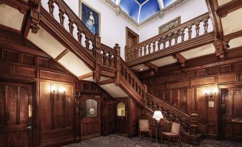 a grand staircase in a large , ornate room with wooden walls and ceiling , flanked by framed pictures at Mercure Bradford Bankfield Hotel