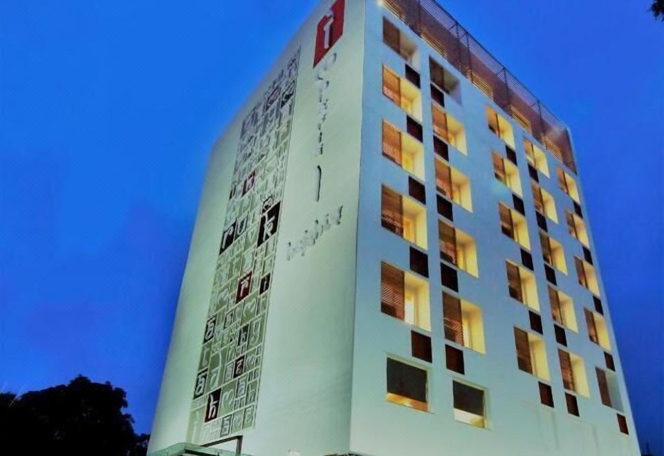 a modern hotel building with a white exterior and large windows , illuminated by lights at night at Imperial Heights