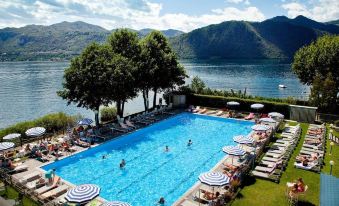 a large swimming pool with people in it , surrounded by lounge chairs and umbrellas , with mountains in the background at Hotel l'Approdo