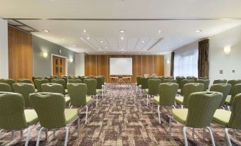 a conference room with rows of green chairs arranged in a semicircle , and a projector screen on the wall at Ramada Plaza by Wyndham Wrexham