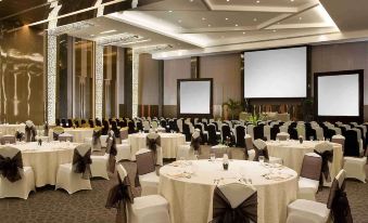 a large banquet hall with multiple round tables covered in white tablecloths and black napkins , set for a formal event at Novotel Bangka - Hotel & Convention Centre