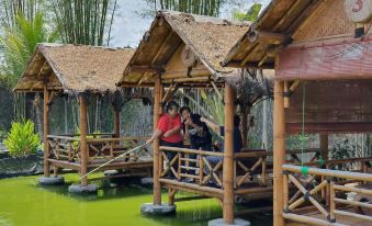 a group of people standing on a wooden platform in front of a green water body , surrounded by bamboo structures at Borobudur Bed & Breakfast