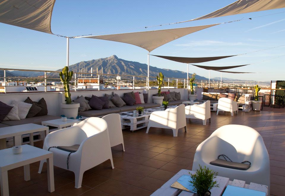 a rooftop terrace with white furniture , including couches and chairs , under umbrellas , offering a view of mountains at NH San Pedro