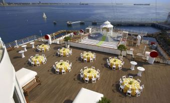 a large outdoor dining area with white tables and yellow chairs is set up on a deck overlooking the ocean at The Queen Mary