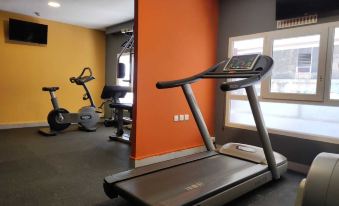 a gym room with various exercise equipment , including a treadmill and stationary bike , in orange and gray colors at Novus Plaza Hodelpa