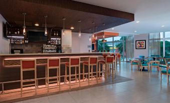 a modern bar with wooden furniture , pendant lights , and multiple bottles on the counter , surrounded by a glass wall at Fairfield by Marriott San Salvador