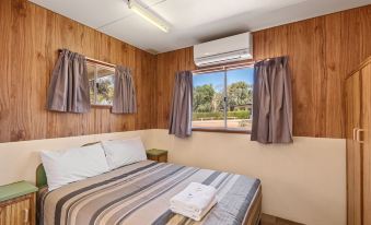 a cozy bedroom with wooden walls , a bed with striped bedding , and two windows with curtains , offering a view of the outdoors at Discovery Parks - Lake Bonney