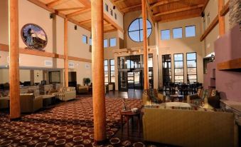 a large hotel lobby with high ceilings , wooden columns , and multiple seating areas , as well as large windows and doors at Moenkopi Legacy Inn & Suites