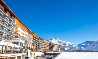 a large building with a modern design is situated in front of a mountain with snow on the ground at Langley Hotel Tignes 2100