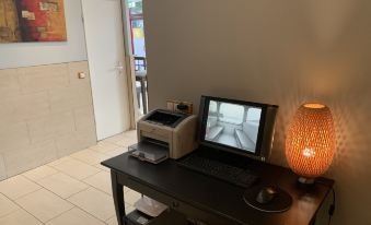 a computer desk with a monitor , keyboard , and printer in front of an orange lamp at Hotel Admiral