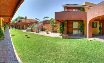 a red - brick house surrounded by green grass and trees , with a paved walkway leading to the entrance at Hotel Hacienda